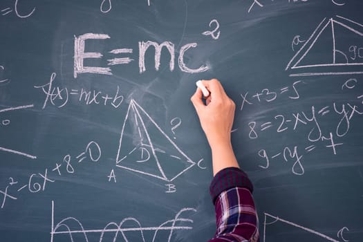 Close-up shot of a hand holding chalk and writing mathematical equations on the blackboard. Education concept.