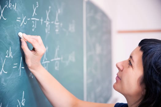 Teacher or student writing on blackboard during math lesson in school classroom.