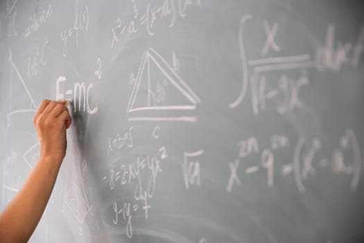 Close-up shot of a hand holding chalk and writing mathematical equations on the blackboard. Education concept.