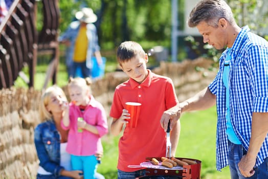 Young man frying sausages on grill outdoors with his son near by