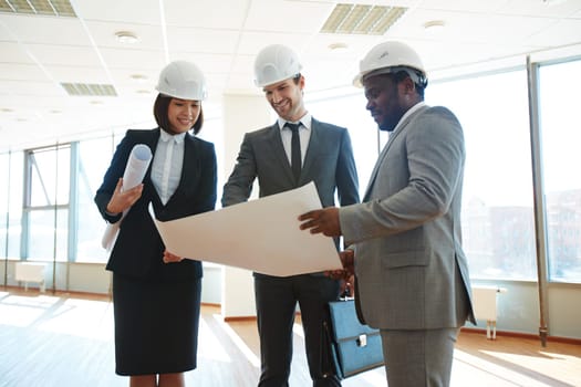 Confident architects in protective helmets discussing blueprint in office