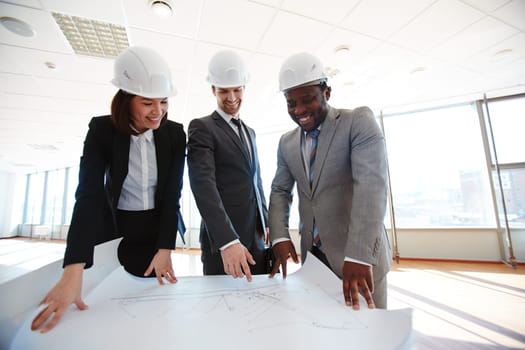 Confident architects in protective helmets looking at blueprint