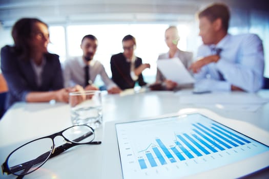 Paper with chart and eyeglasses on background of business colleagues