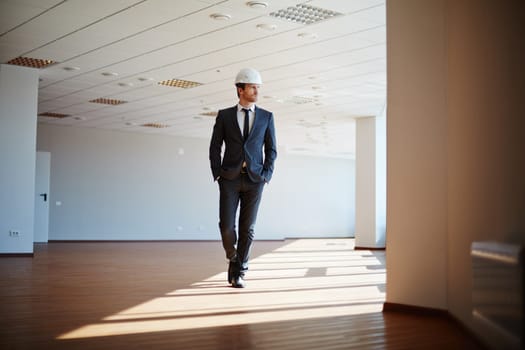 Male architect in suit and helmet walking along office
