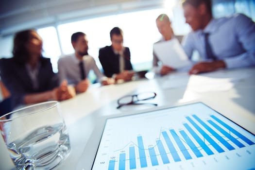 Paper with charts and glass of water on background of working colleagues