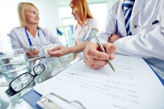 Close-up of doctor with pen filling in personal data