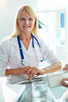 Happy young woman in white coat looking at camera at workplace