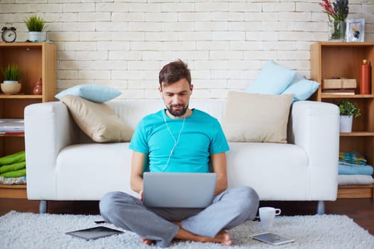 Handsome guy with earphones using laptop at home