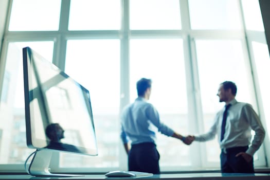 Computer monitor at workplace with two male colleagues handshaking on background