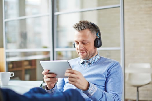 Handsome businessman with earphones and touchpad having break