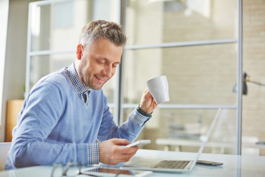 Businessman with cup of coffee reading sms on cellphone before meeting