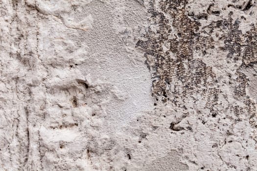 Rough texture of an ancient block of stone part of an external wall. Cavernous rock structure with brittle surface. Pale gray and beige colors with dark streaks. Close up shot outdoors on a tripod.