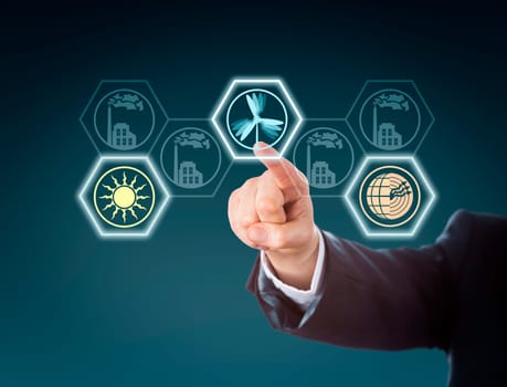 Arm in corporate suit raising index finger to push a wind energy button in touch screen interface. Wind, solar and geothermal power icons lighting up, while traditional power stations remain inactive.