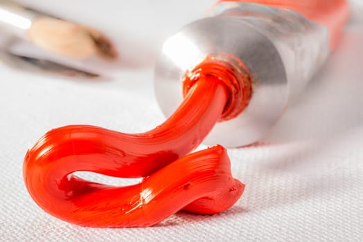 Scarlet Lake orange oil paint squirted from tube on to a white canvass.
