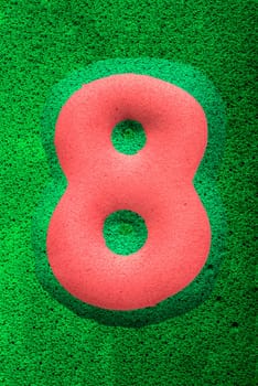 The number eight in a red sponge like texture, raised 3D from the green background.