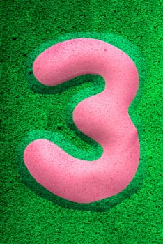 The number three in a pink sponge like texture, raised 3D from the green background.