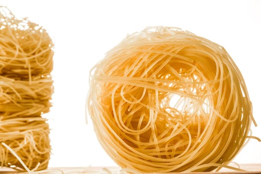 A role of angel's hair spaghetti infront of a white bacground, with three more roles stacked on top of each other to the left.
