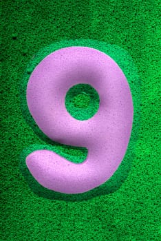 The number nine in a purple  sponge like texture, raised 3D from the green background.