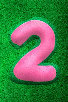 The number two in a pink sponge like texture, raised 3D from the green background.