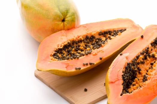 Papaya halved with a longitudinal cut. Succulent orange colored fruit pulp and peppery dark seeds. Fruit of the tropical Carica papaya. Close up with selective focus. Studio shot on white background.