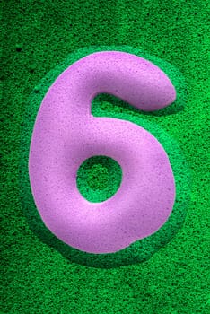 The number six in a purplesponge like texture, raised 3D from the green background.