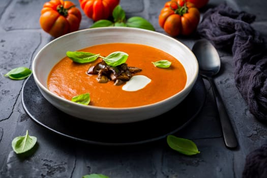 Homemade tomato soup with roasted eggplant and basil on dark background
