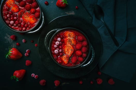 Breakfast red smoothie bowl with chia seeds, strawberry, raspberry and redcurrants on black background