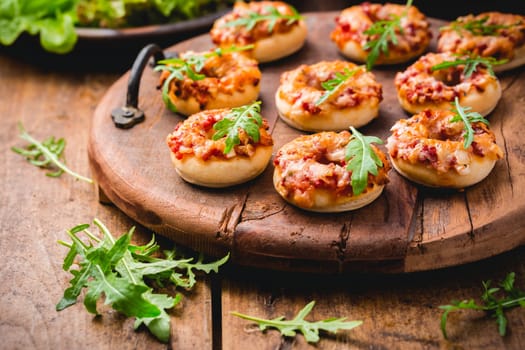 Small pizza in donut shape with rocket (arugula) and fresh salad on wooden background