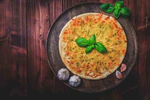 Pizza bread with garlic, cheese and basil on wooden background
