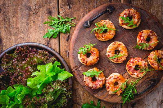 Small pizza in donut shape with rocket (arugula) and fresh salad on wooden background