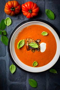 Homemade tomato soup with roasted eggplant and basil on dark background