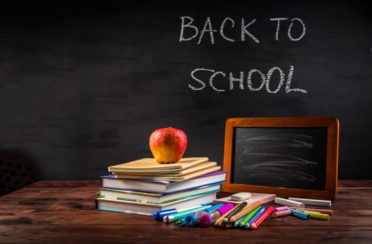 Pile of book and exercise books with school applies and apple snack with chalkboard. Back to school concept.