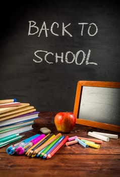 Pile of book and exercise books with school applies and apple snack with chalkboard. Back to school concept.