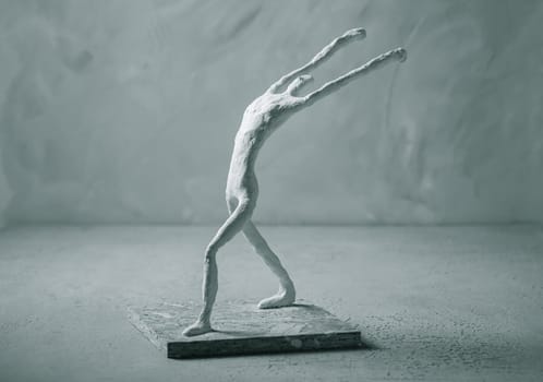 Plaster sculpture of sportsman in winner pose on concrete background in grey tones.