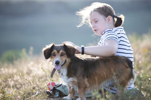 Child with her dog sitting and  in summer meadow