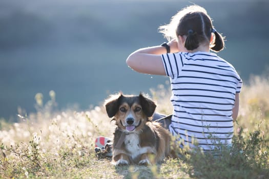 Child with her dog sitting and  in summer meadow