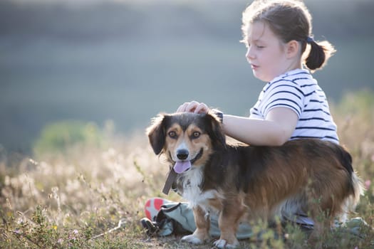 Child with her dog sitting and  in summer meadow