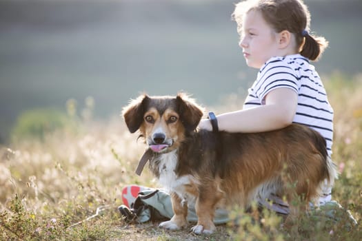 Child with her dog sitting and  in summer meadow