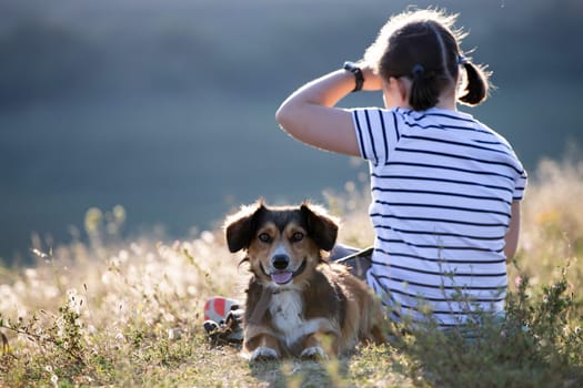 Child with her dog sitting and  in summer meadow