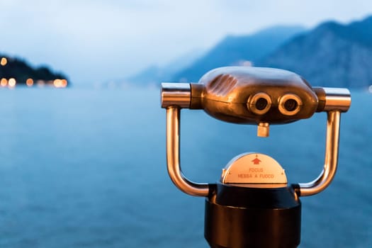 Tourist binoculars on the lake Lago di Garda, evening scene with water and mountains