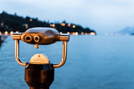 Tourist binoculars on the lake Lago di Garda, evening scene with water and mountains
