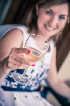 Beautiful young girl with blond hair holds a glass of wine and smiles, holidays