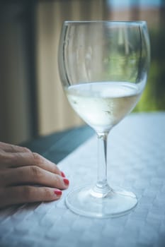Glass of white wine and hand of a woman on a table