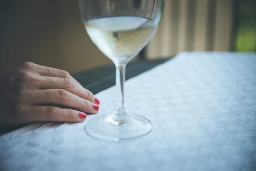 Glass of white wine and hand of a woman on a table