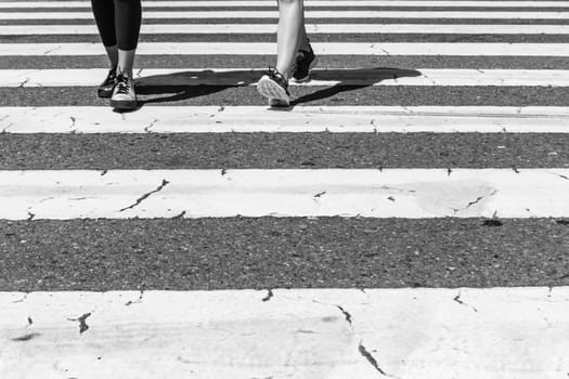 Legs, feet and shoes from two young women walking on town street crosswalk in a hurry pace urban day lifestyle. Black and white style.