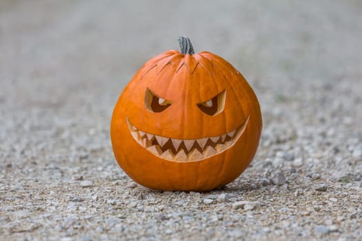 Big scary smiling halloween pumpkin with fiendish smile sitting on the floor outdoor. Spooky nightmare mystery scene at ocober 31st.