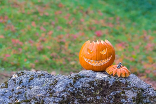 Big scary smiling halloween pumpkin with demon smile sitting alone in twilight nature. Spooky nightmare mystery scene at ocober 31st.