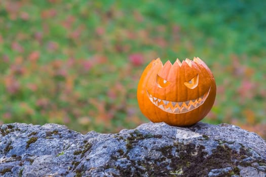 Big scary smiling halloween pumpkin with demon smile sitting alone in twilight nature. Spooky nightmare mystery scene at ocober 31st.