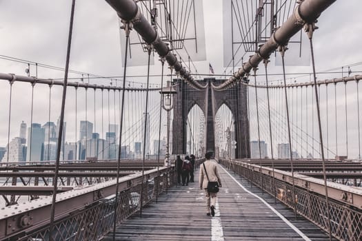 Man walking on pedestrian path across Brooklyn bridge. New York City Manhattan downtown with skyscrapers over East River panorama as seen from Brooklyn bridge.