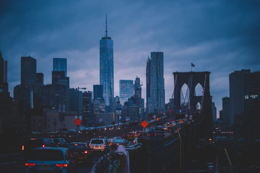 Traffic on Brooklyn bridge and New York City Manhattan downtown skyline at dusk with skyscrapers over East River panorama.